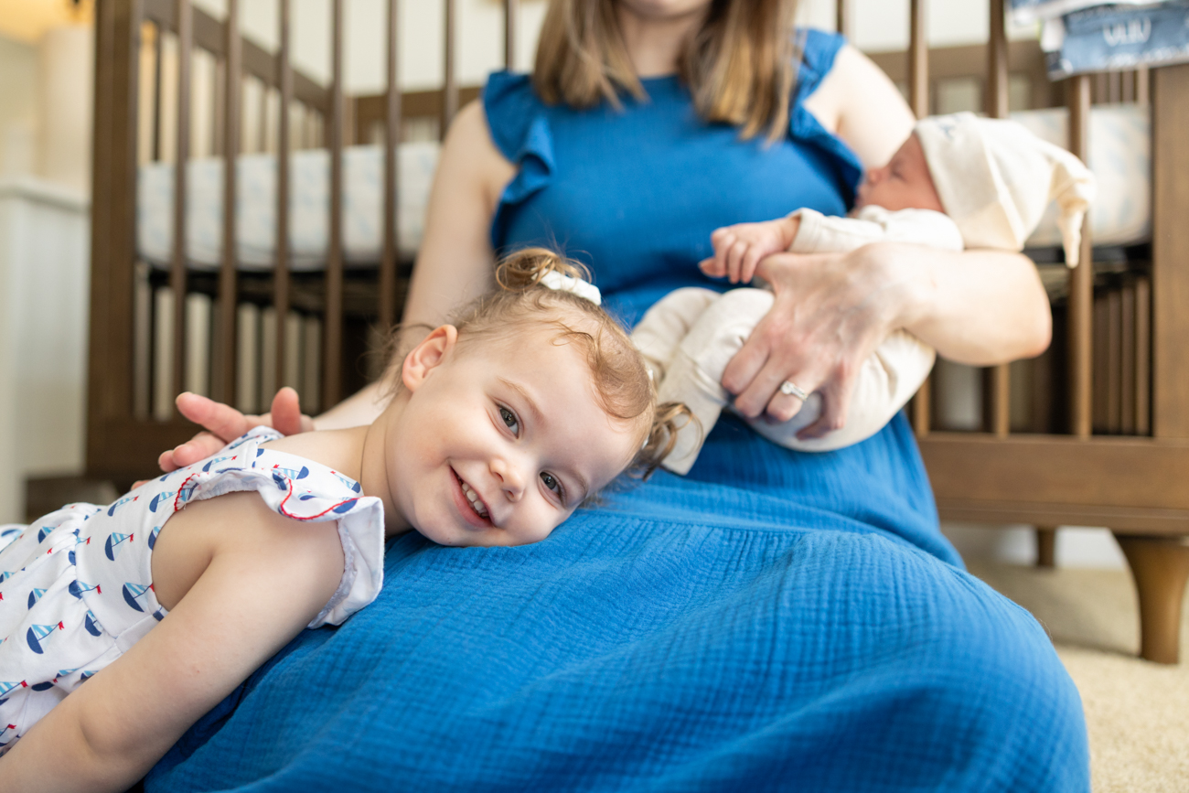 newborn-session-with-toddler Close up of a toddler girl laying on mom's lap, while mom hold newborn baby