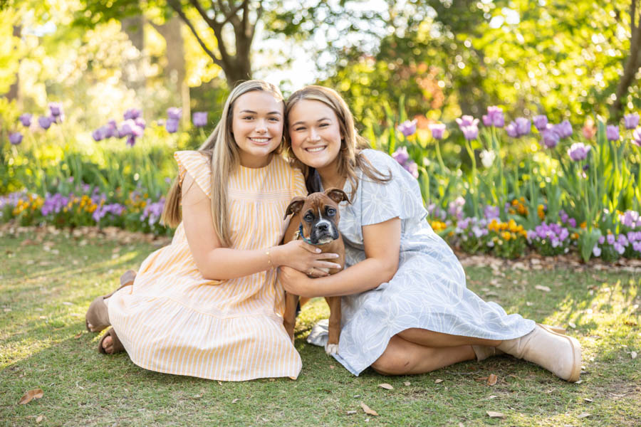 Two teenage girls in sundresses at a park in spring with their boxer puppy